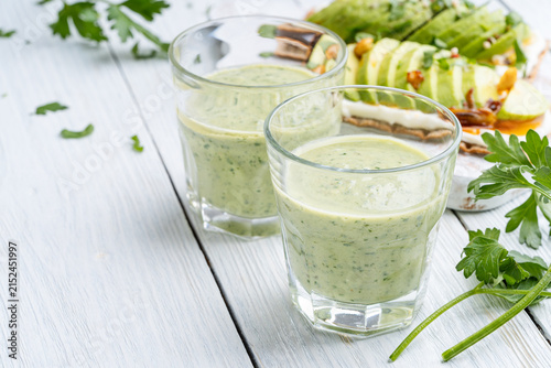 Avocado smoothie in glasses on white wooden background