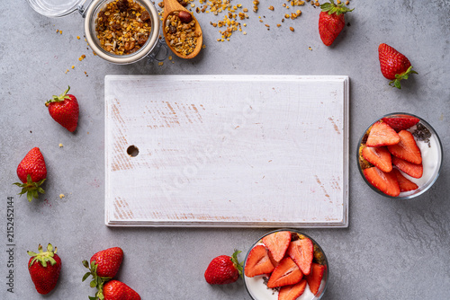 Homemade gluten free granola with yoghurt, chia seeds, and fresh strawberries in glasses, healthy breakfast, white wooden board for recipe