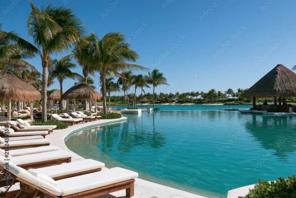 Fototapeta premium Turquoise Caribbean resort pool under palm trees with sun loungers and cabanas in Cancun
