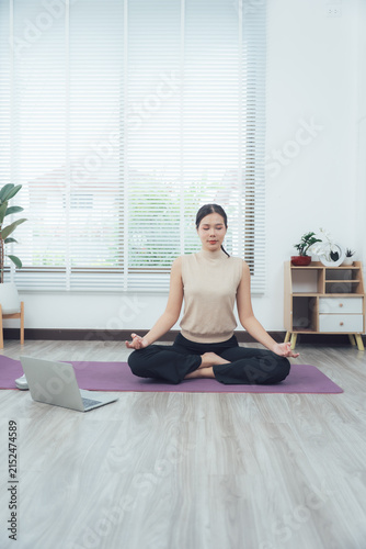Foto Zen Moment at Home: A serene young woman in a meditative pose finds inner peace as she practices yoga in her bright, airy living room, guided by an online instructor on her laptop