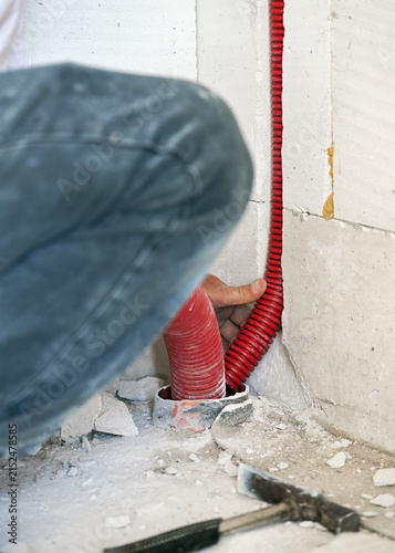 Construction worker builder installing plastic pipes for electric cables into wall and floor