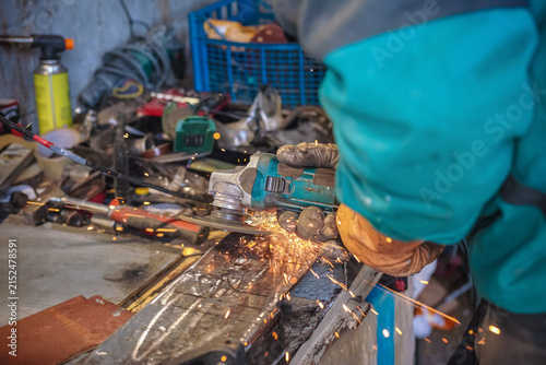 Working with rotary angle grinder at workshop, adjusting metal car part, closeup detail, orange sparks flying around
