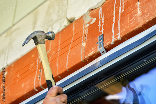 Construction worker securing window frame before installation in brick wall with a hammer