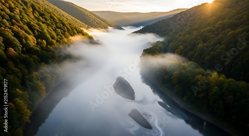 Misty river valley at sunrise with sun rays breaking through trees and fog over water