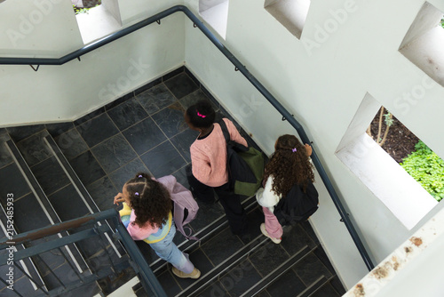 African American child and two teenage females descending stairwell, holding backpacks and rail