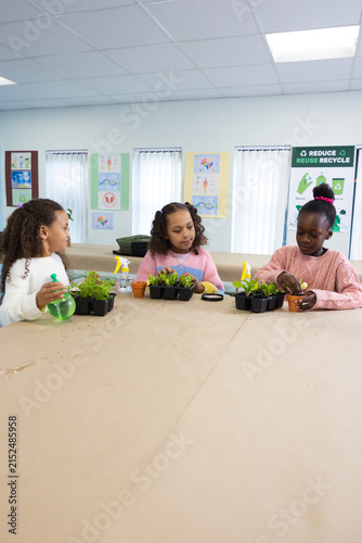 African American child and teen girls planting seedlings at craft table in classroom using pots