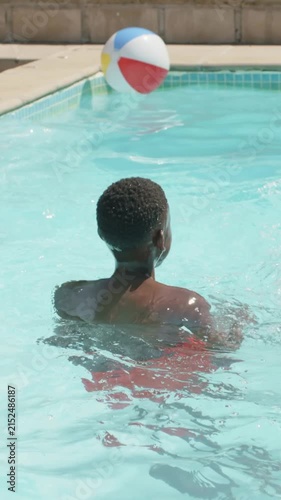 Vertical video: Drifting ball on edge making teen turning, reaching ball in red trunks at home pool