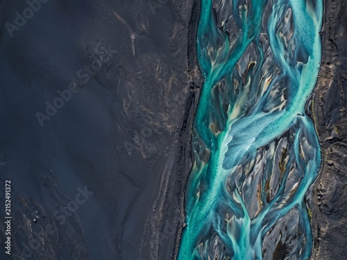 Aerial top-down view of turquoise glacial river streams flowing through dark volcanic sand in Iceland, creating abstract natural patterns