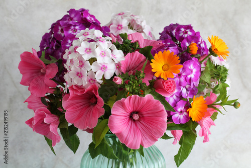 Colorful bouquet of pink lavatera, purple phlox and orange calendula flowers in glass vase