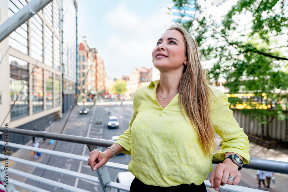 Fototapeta premium Woman enjoys the view on a city balcony on a sunny day while looking up and smiling