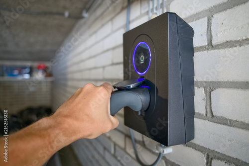 Foto close up of hand plugging electric vehicle charging cable into home wallbox char