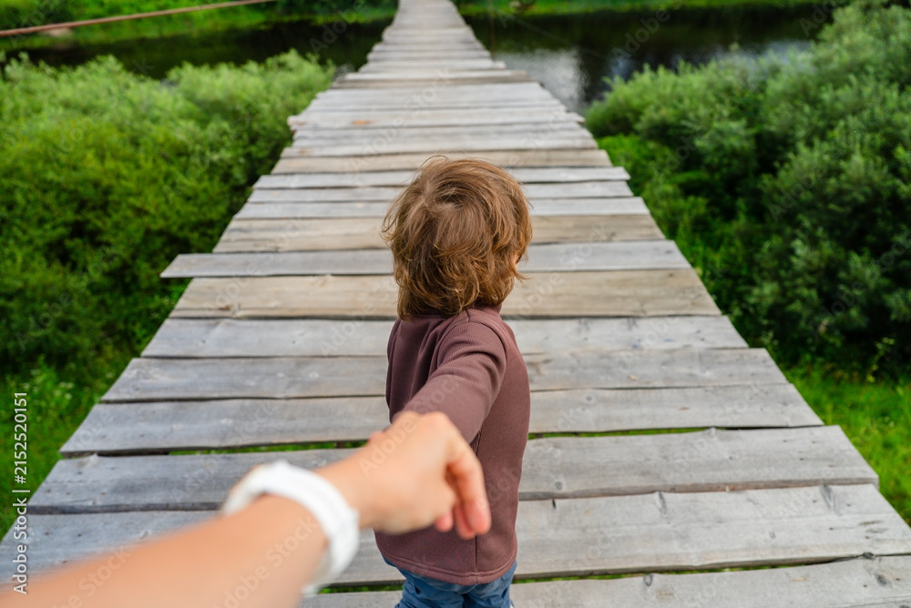 Obraz premium Caring mother holds her little boys hand while guiding young explorer across scenic wooden bridge in nature. This moment captures deep trust and parental protection as they discover outdoors together