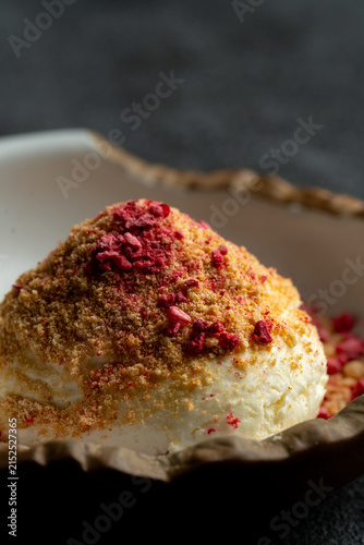 A dessert is placed in a bowl. It has a smooth base covered with crushed toppings. The setting is simple and focuses on the dessert itself without any distractions