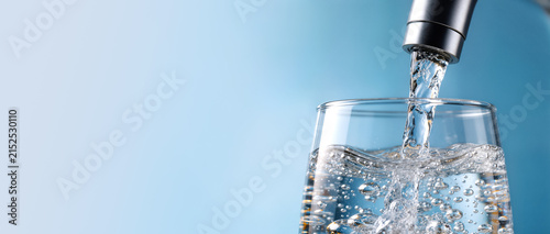 Crystal clear water pouring into a glass against a bright blue background, symbolizing freshness and purity