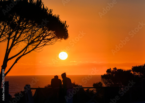 Couple watching the sunset on La Barrosa beach, Chiclana, Spain.