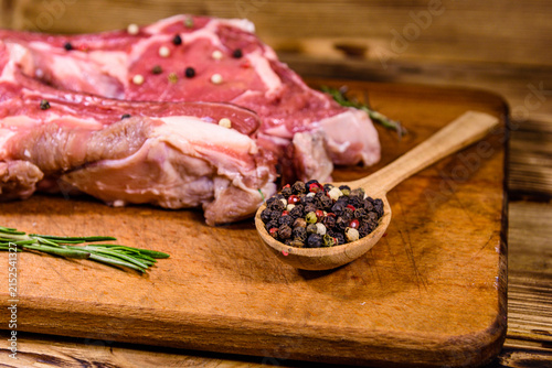Raw ribeye steak, wooden spoon with spices and rosemary on a cutting board