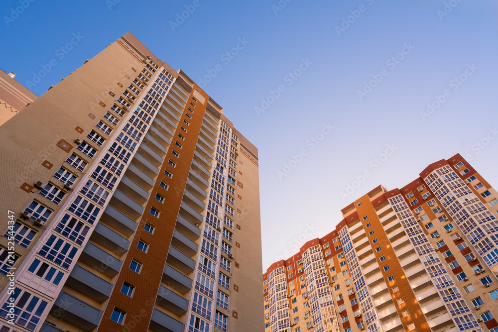 Fototapeta premium Low angle view of modern high rise residential apartment buildings in complex with windows and balconies against clear blue sky in modern city district