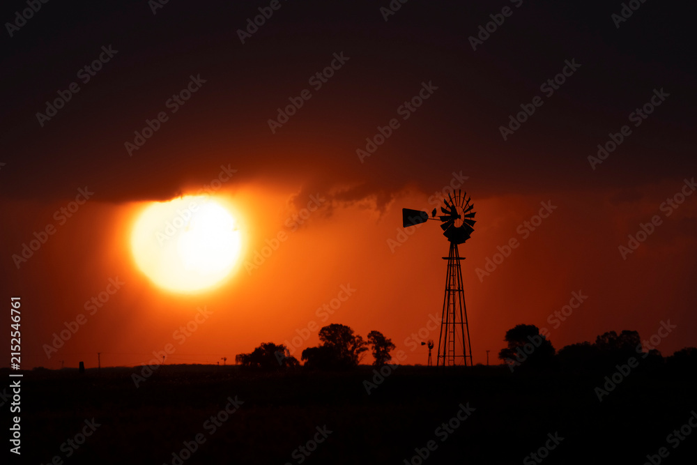 Naklejka premium Windmill at sunset with a rain storm in the background, Pampas, Patagonia,Argentina.