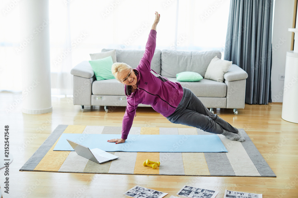 Fototapeta premium Senior woman exercise stretching yoga using laptop online instructions at home health care