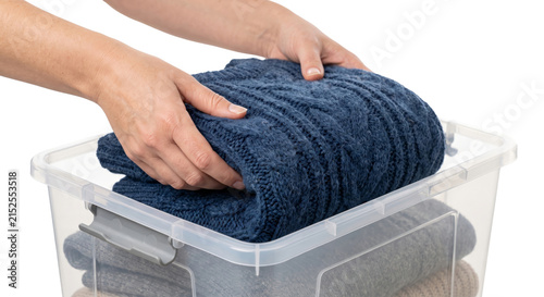 Fotografie Hands folding a warm blue knitted sweater into a clear plastic storage bin