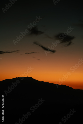 Dark mountain silhouette beneath a glowing orange twilight sky after sunset in Joshua Tree National Park, California