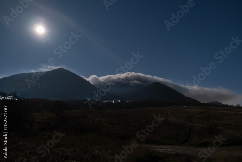 Fotografie A beautiful view of mountain peaks in the fog and the mon in the night sky