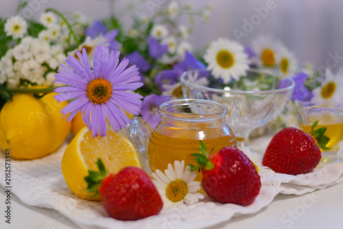 Fresh strawberries, golden honey, bright lemon and blooming daisies create a cozy farmhouse breakfast composition. An empty glass dessert bowl is ready to be filled with wholesome seasonal ingredients