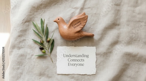 Elegant wooden dove figurine with Common Ground text on wing beside olive branch and note card saying Understanding Connects Everyone on linen background symbolizing peace and global unity for people.
