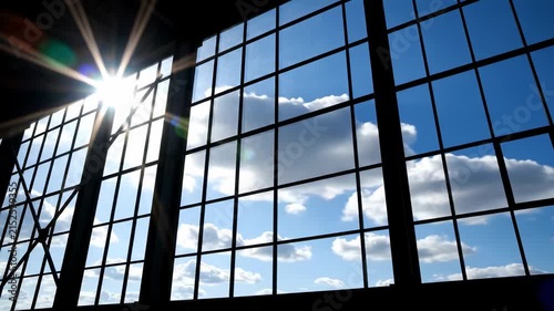 Bright Sunlight Through Industrial Windows with Blue Sky and Clouds, Ideal for Corporate Backgrounds.