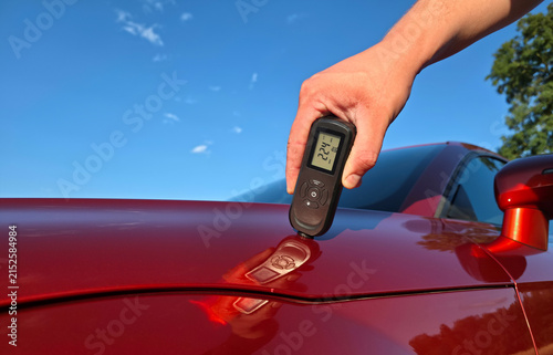 Man using paint thickness gauge to check car hood coating before buying used vehicle