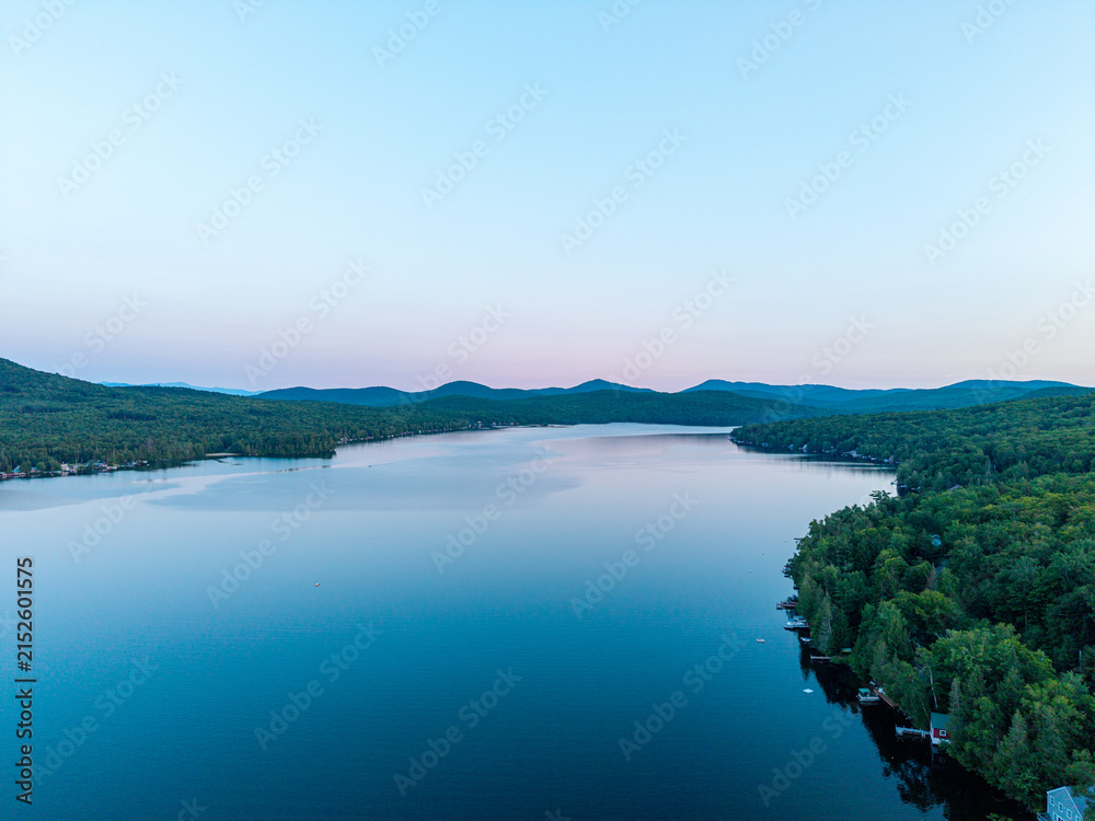 Fototapeta premium Maidstone Lake, Vermont, high aerial drone view at dusk, showing calm waters reflecting the soft twilight sky over surrounding mountains and forested shorelines.