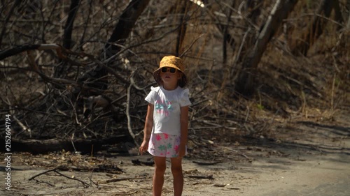 A little girl looks with interest aftermath of a forest fire, trees without leaves and branches, dead wood, asks and inquires about the reasons, turns her head, a sunny spring day.