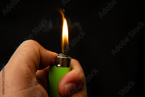 Hand holding a burning green lighter on a black background.