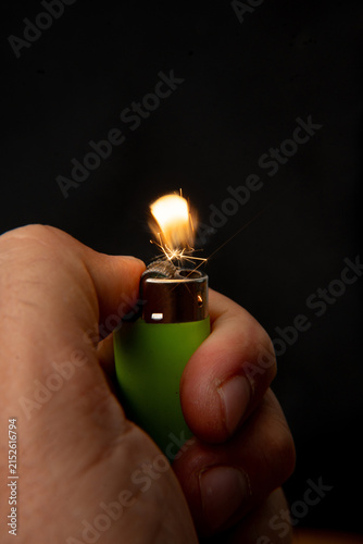 Hand holding a burning green lighter on a black background.