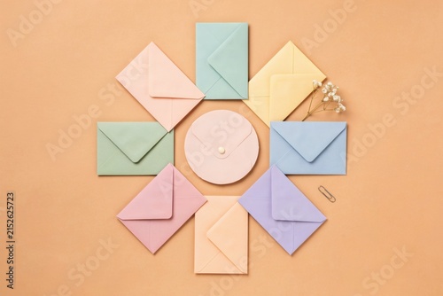 Pastel colored envelopes arranged in a circle with a DVD disc on a peach background, flat lay composition with dried flowers and paper clip, office stationery concept