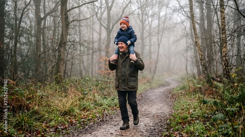 A happy man carries a smiling boy on his shoulders through a foggy autumn forest path.