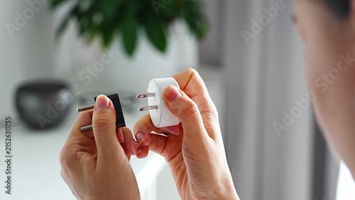 Woman compares electrical plug adapters for different power outlets at home. International travel and power compatibility concept for global electronics.