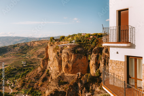 White building featuring traditional Spanish architecture with balconies offering a high angle view of the dramatic El Tajo gorge. Surrounding valley. And mountains under a clear sky in Ronda. Spain