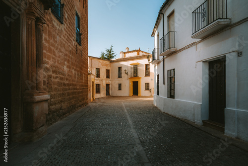 Ronda's old town street features traditional Andalusian architecture, showcasing historic buildings with white facades and an ancient stone pavement under a clear sky