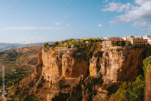 Ronda's iconic white buildings and historical architecture are sitting precariously on top of towering natural cliffs, offering breathtaking views of the valley and surrounding Andalusian landscape
