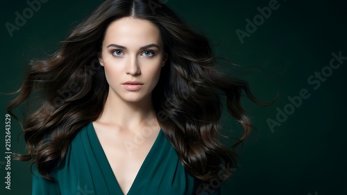 Portrait of a young woman with long dark wavy hair wearing a dark green dress against a dark green background