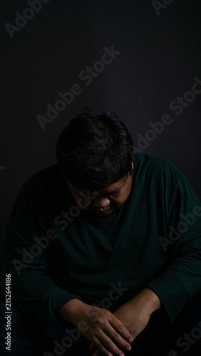 фотографія A deeply sorrowful portrait of a defeated Southeast Asian male sitting with the head bowed completely down against a pitch black background
