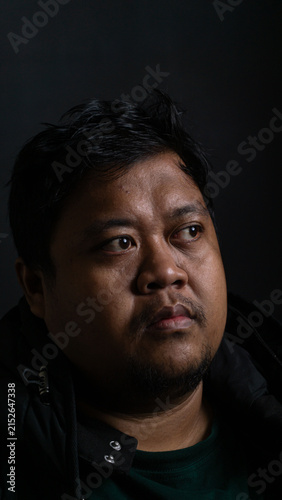 Canvastavla A detailed portrait featuring a serious Southeast Asian male glancing towards the right side against a pitch black background