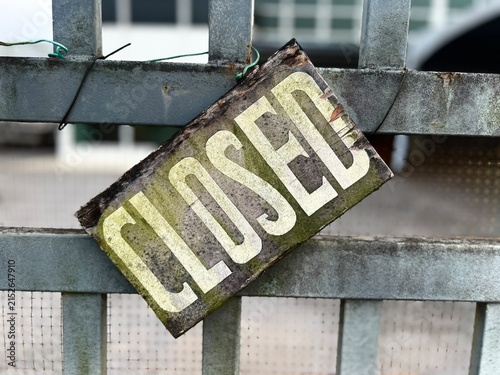 Foto A weathered wooden closed sign attached to a metal security gate outside a business premise