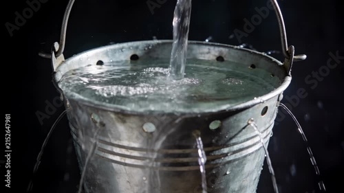 Water pouring into a bucket and escaping from many holes