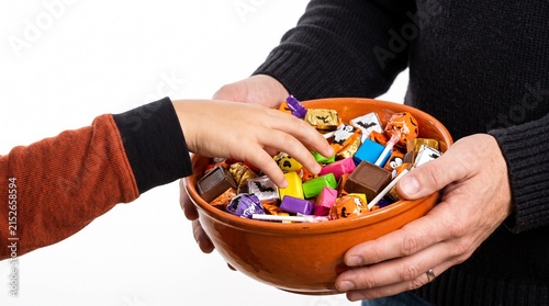 Childs hand reaching into a bowl of Halloween candy held by an adult