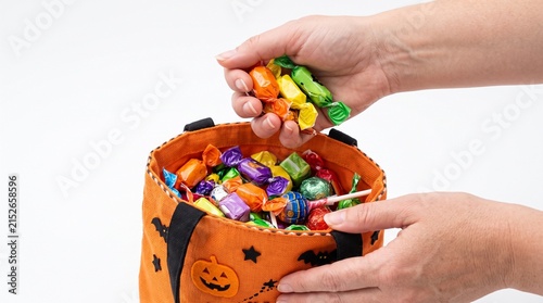 Hands holding a Halloween candy bag filled with colorful assorted candies and a person adding more sweets