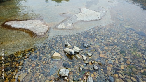 Clear shallow stream flowing over smooth rocks and pebbles in nature.