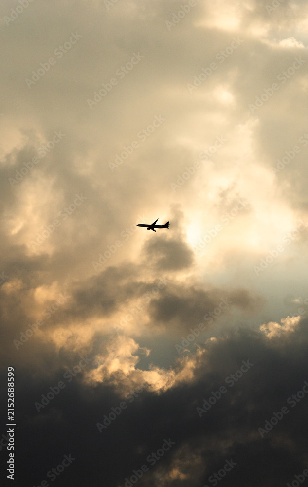 Fototapeta premium Silueta de avión volando a través de nubes dramáticas al atardecer | Airplane silhouette flying through dramatic clouds at sunset