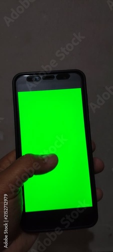 Close up of hand holding smartphone with green screen in landscape mode.